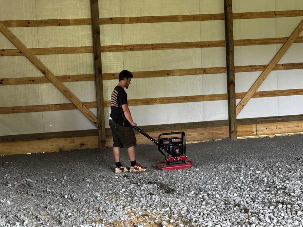 Worker compacting gravel base inside a barn